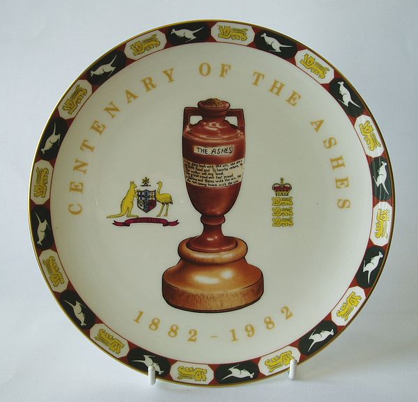 A Coalport china plate bearing a central image of the Ashes urn, with decorations on each side, with printed title and decorative border.